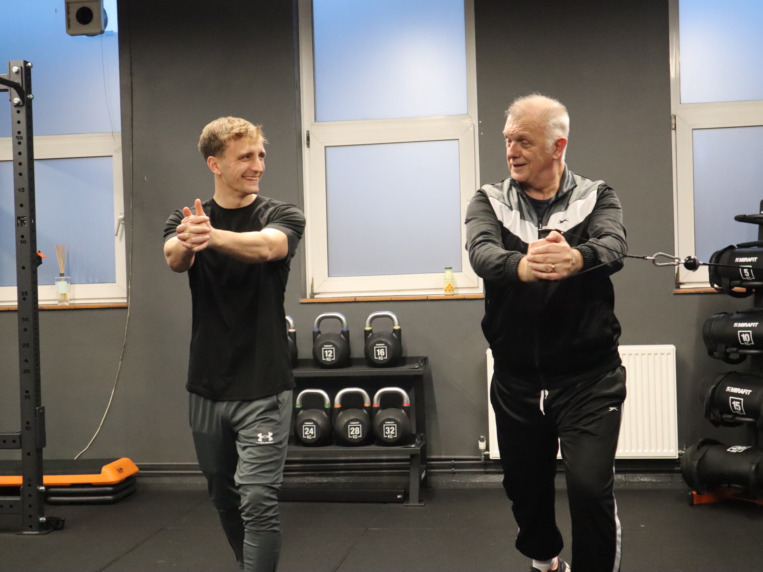 A coach guiding an older member through a warm-up stretch